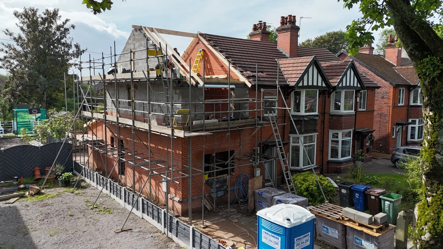 Two-storey brick extension with scaffolding and a timber roof structure under construction
